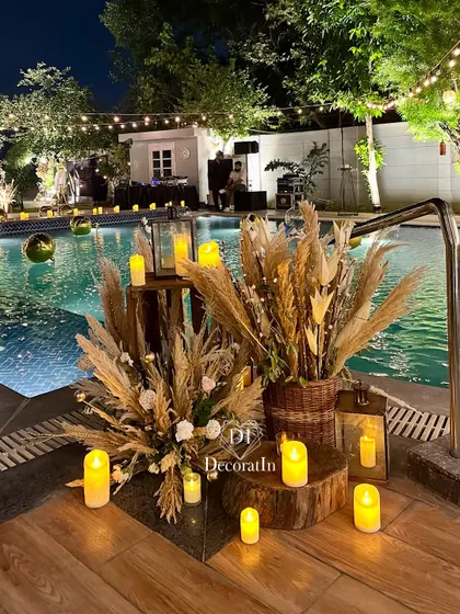 A close-up of the poolside decor, showing the mix of textures from the wicker basket, dried florals, and the warm glow of the candles.