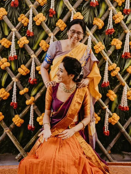 A lovely portrait of the bride and her mother during a Haldi ceremony, with a traditional bamboo and marigold backdrop.