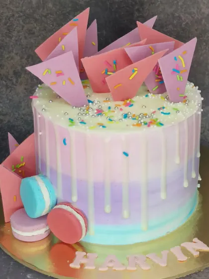 A beautiful pastel cake with chocolate shards and macarons. This fresh whipped cream chocolate cake has a modern and artistic design.