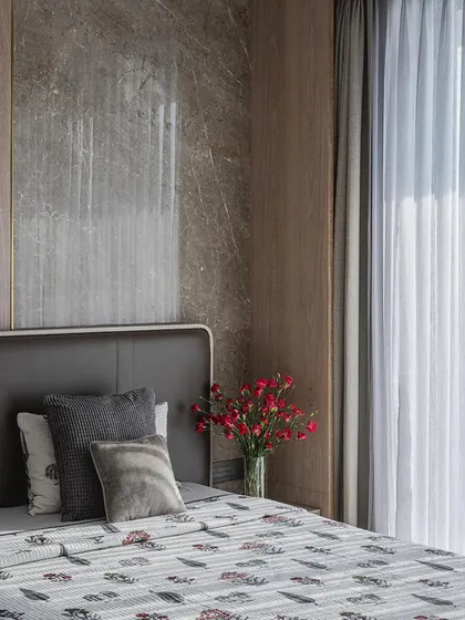 A detail shot of the bedside in a neutral-toned bedroom, showing the mix of textures between the marble wall, wood paneling, and soft bedding.
