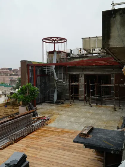 A wide shot of the Pitampura terrace during construction. This image gives a sense of the scale of the project, with multiple structures like the pergola and spiral staircase being built.