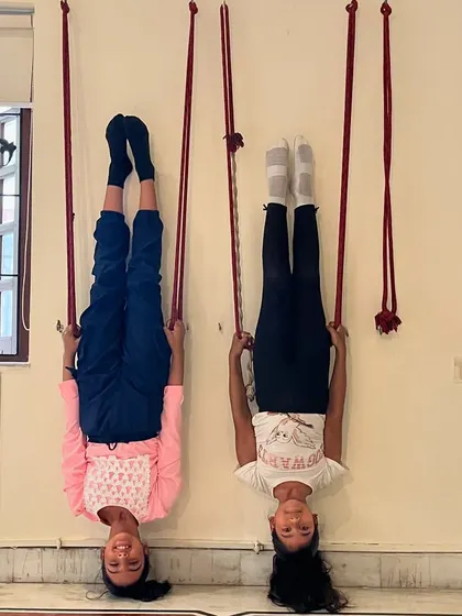 A duplicate of image 13, showing two students in a happy, inverted pose using wall ropes.