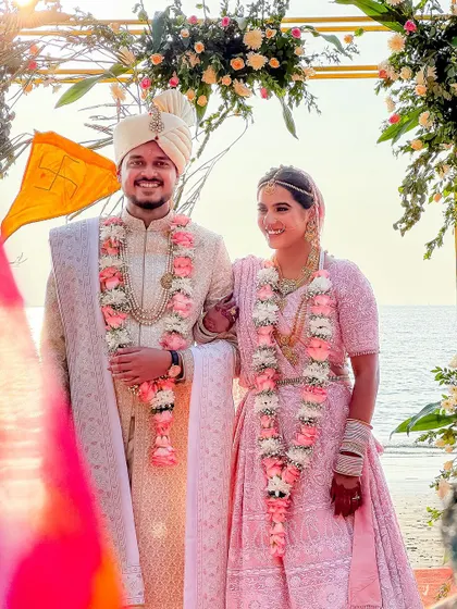 A beautiful portrait of the couple standing under their wedding arch on a Goa beach, with the ocean behind them.