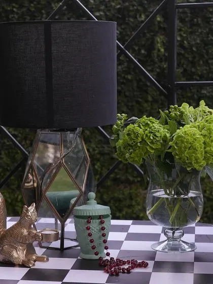 A quirky detail of a golden squirrel figurine on a checkerboard table, next to a modern lamp and a vase of green hydrangeas.
