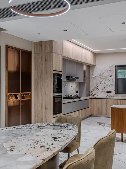 The kitchen is designed as part of an open-plan living and dining area, with the materials and colors of the kitchen complementing the dining furniture for a cohesive design.