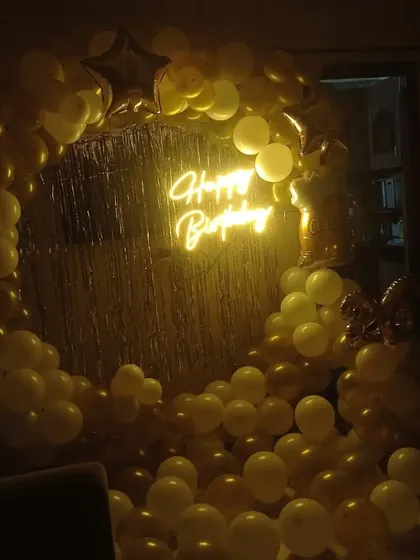 A golden balloon ring with a neon sign and shimmer curtain, seen here in a dimly lit room. The lighting creates a warm and intimate party atmosphere.
