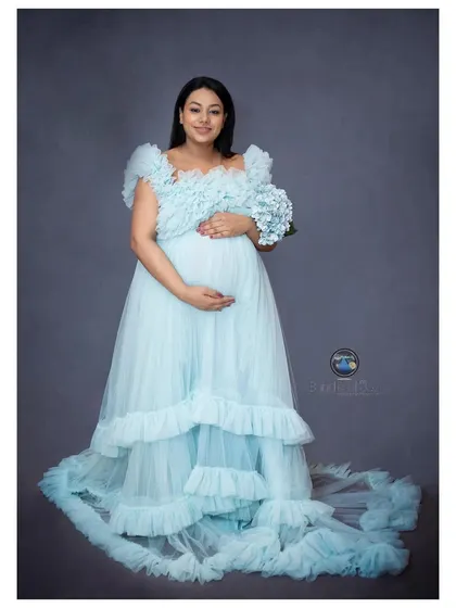 A full-length shot of an expecting mother holding a bouquet of blue hydrangeas, perfectly complementing her gown and hinting at the joy to come.