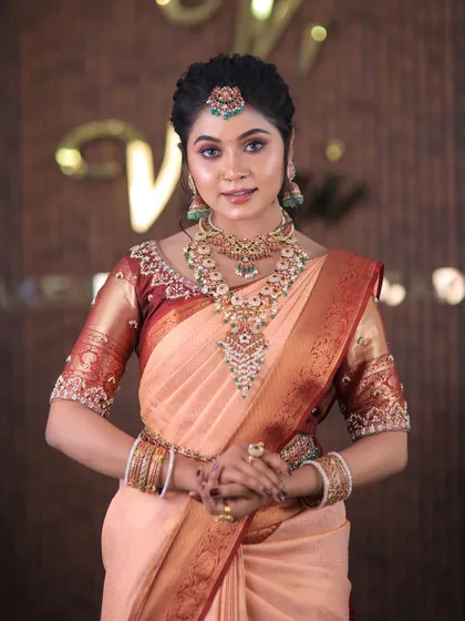 A full set from a photoshoot featuring a lovely peach-colored silk saree. The drape is kept simple and elegant to highlight the beautiful color and the intricate temple jewellery.