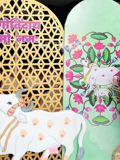 A decorative corner featuring traditional Pichwai art style. A cutout of a sacred cow and a panel with lotus motifs were paired with a golden jaali screen, blending cultural art with event decor.