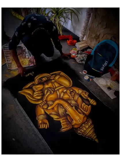 A rangoli artwork of Lord Ganesha, or Bappa, created for Ganesh Chaturthi celebrations at the Karnataka Chitrakala Parishad in Bangalore. The golden tones and intricate form on a black background make the deity stand out.