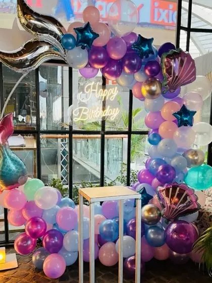 An enchanting mermaid theme for a first birthday. The balloon arch is decorated with mermaid tail and seashell foils, complemented by a neon sign and a light-up number '1'.