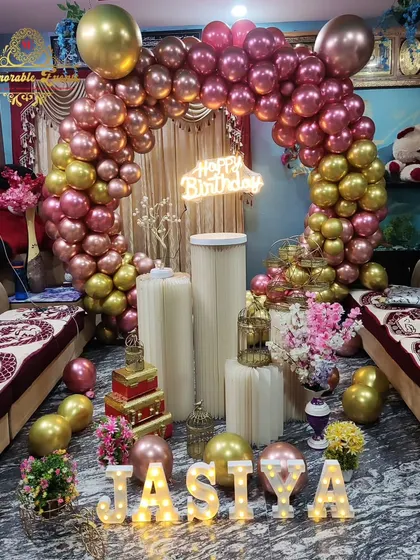 A birthday setup with rose gold and pink balloons, featuring a modern slatted circular backdrop.