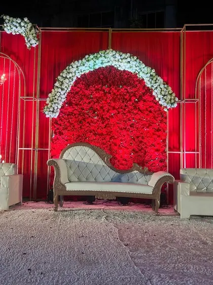 A centered shot of the all-red wedding stage, focusing on the main seating area. The symmetrical design with the central floral arch makes for a perfect photo backdrop.
