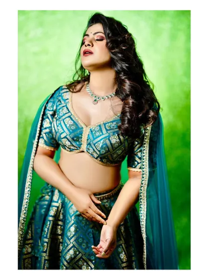 A striking portrait of a model in a teal blue brocade lehenga. The rich color and traditional pattern make it a standout choice for any festive occasion.