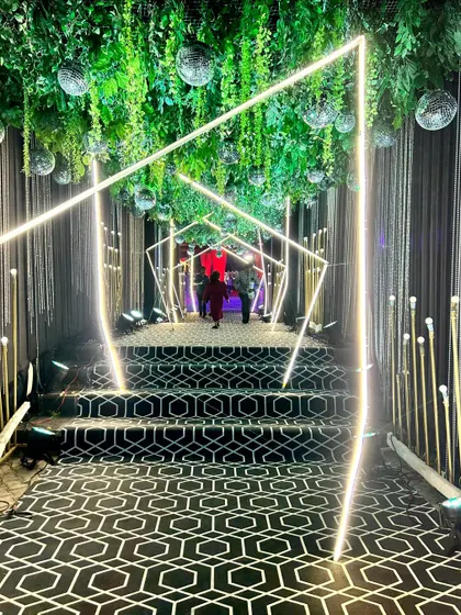 We guide your guests through a mesmerizing geometric tunnel of light for a truly modern and glamorous Sangeet entrance. This immersive walkway, featuring a custom patterned carpet and hanging greenery, sets a sophisticated and high-energy tone for the evening.