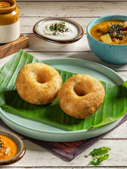 Crispy Medu Vada served on a banana leaf with sambar and coconut chutney, capturing a classic South Indian snack.