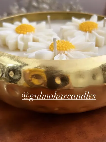A close-up of the unlit daisy urli candle, showing the detail of the hammered gold metal and the wax flowers.