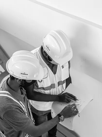 A black and white, top-down view of two engineers collaborating over a blueprint. This captures a moment of focus and teamwork that defines our on-site process.