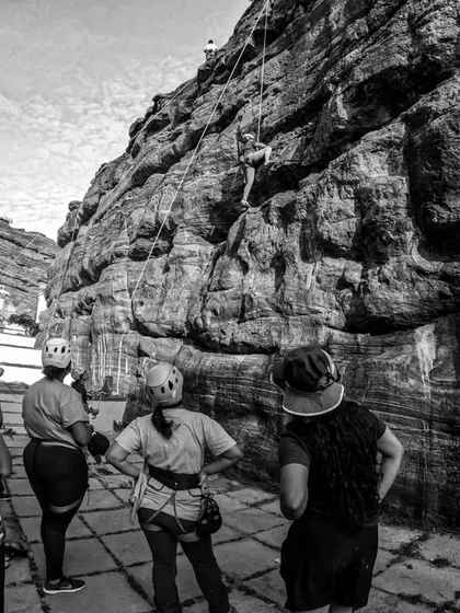 The same epic scene in black and white, highlighting the textures of the rock and the focused attention of the participants learning the ropes.