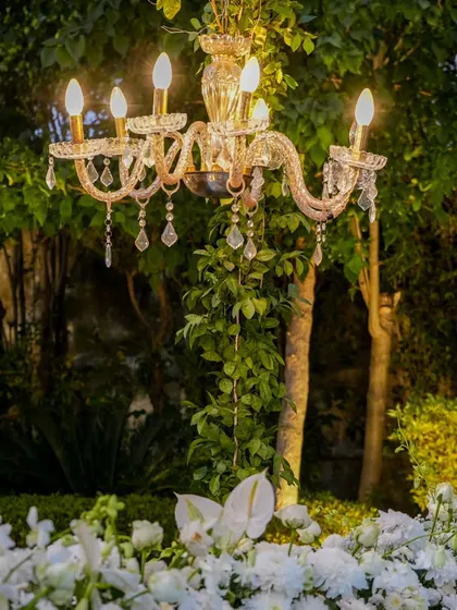 A classic crystal candelabra emerges from a bed of white flowers, adding a touch of old-world glamour and warm light to the garden setting as evening approaches.