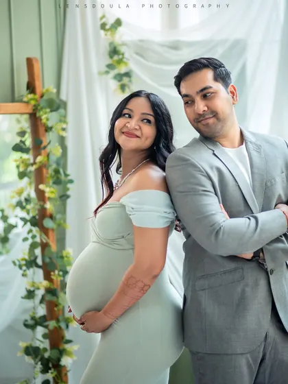A playful and chic pose with the couple back-to-back. The soft green tones and natural light from the window create a fresh and airy feel for this indoor maternity shoot.
