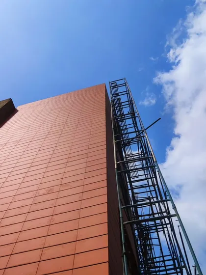 An upward shot of the Arihant Aspire clubhouse facade under construction, showing the terracotta tiles against a blue sky.