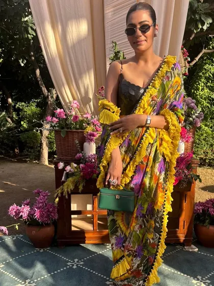 A fun and vibrant look in a yellow floral Shivan & Narresh saree with a ruffled border. Paired with a green bag, it's a perfect outfit for a daytime wedding event.