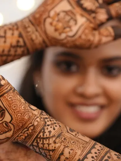 A creative shot of the client peeking through her hennaed hands, highlighting the beautiful patterns.