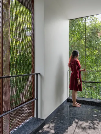 A balcony in the Copper House offers a framed view of the lush green surroundings. The perforated steel screens create a sense of enclosure and privacy while maintaining a visual connection to the outdoors, demonstrating our focus on creating layered thresholds.