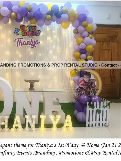 A simple and elegant theme for a first birthday at home. The decor features a backdrop of fairy lights, a purple and gold balloon arch, and a "ONE" table, creating a warm and magical setting.