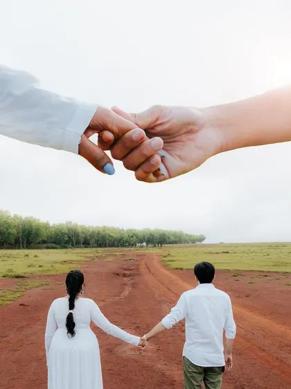 A creative shot symbolizing the journey ahead. The couple walks down a long country road, with their hands clasped together in the foreground, representing their bond.