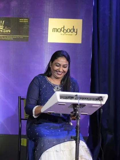 One of our faculty members, Priya Madam, smiling as she plays the rhythm pad, providing musical support for the students' Shiva Bhajan performance.