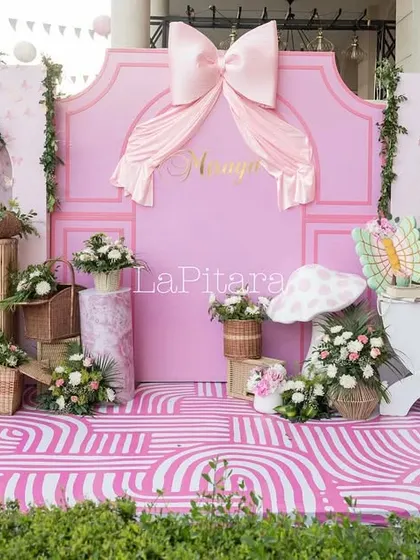 The main stage for the bow-themed party, featuring a large pink backdrop, butterfly wing props, and a dessert cart.