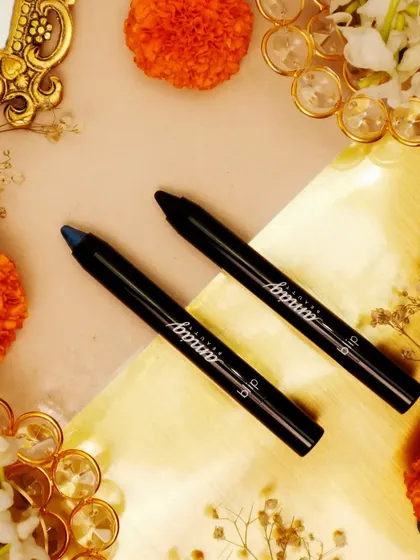 A festive flatlay featuring eye pencils surrounded by marigold flowers and decorative gold elements. The warm, vibrant colors are perfect for a Diwali-themed beauty campaign.