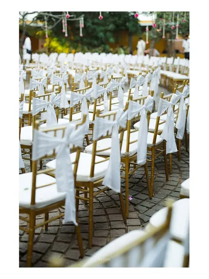 Elegant gold Tiffany chairs are decorated with simple white bows for this outdoor ceremony. This small detail adds a touch of sophistication and unifies the guest seating area.