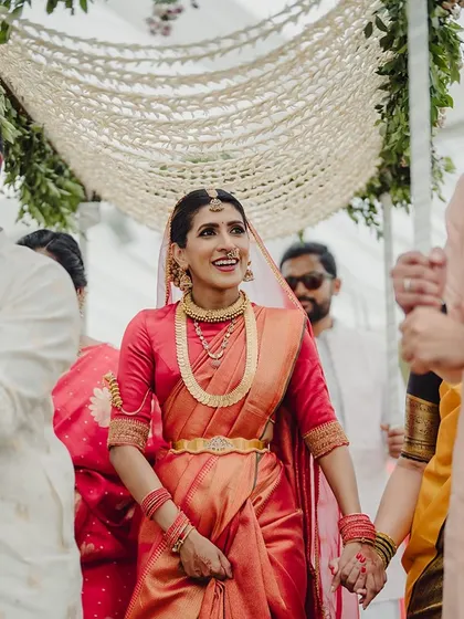 A beautiful bride in a traditional red saree makes her way through the wedding festivities, her smile lighting up the event.
