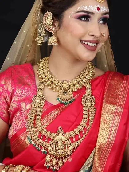 A happy bride combining Bengali and South Indian styles, wearing a heavy temple jewellery set with a traditional Bengali 'kanbala' earring.