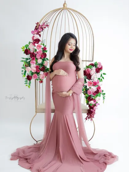 A beautiful portrait in a dusty pink gown. The mom-to-be is seated in a golden birdcage chair, creating a regal and romantic image.