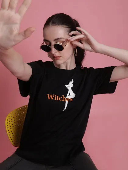 A close-up shot focusing on the 'Witches' graphic tee. The styling is simple to let the t-shirt's quirky design and the model's expression take center stage.