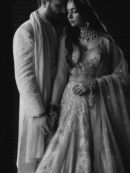 A dramatic, low-key black and white portrait. The focused lighting highlights the texture of their outfits and the intimate connection between the couple.