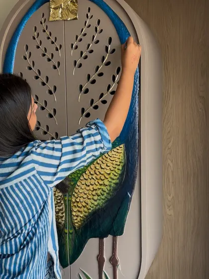 A close-up of the hand-painted peacock art on a wardrobe door, showing the detailed feather work and the application of gold leaf. This turns a simple door into a luxurious art piece.