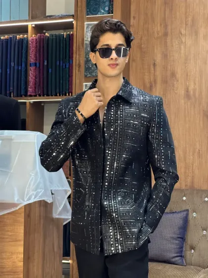 A client posing in a black sequined jacket in our store. The background of fabrics and sewing machines tells the story of our craft.