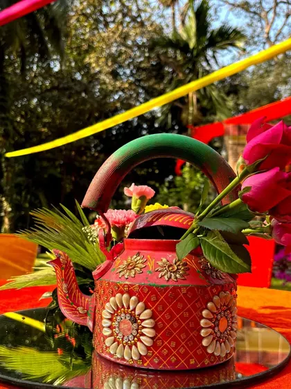 A quirky and colorful centerpiece for a Mehendi, using a hand-painted kettle filled with bright red roses.