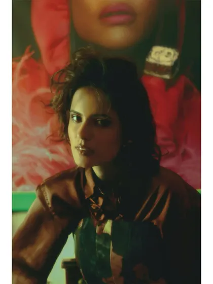 A powerful close-up where the model is framed against a portrait in the background, creating a dialogue between the subject and her own idealized inspirations.