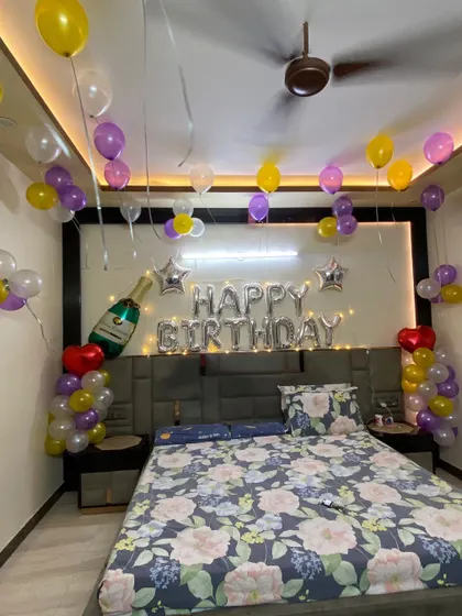 This birthday room setup features a fun champagne bottle foil balloon, star accents, and a colorful mix of yellow, purple, and white balloons, all complemented by warm fairy lights.