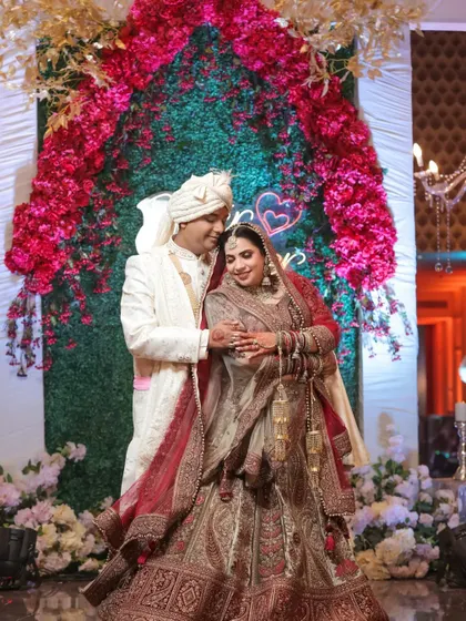 A beautiful wedding portrait of a couple under a floral arch. The groom's hand gently holding the bride's arm shows their new bond.