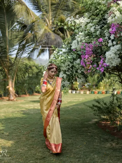 The bride walking through a lush garden in Goa, her golden saree shining in the sun.