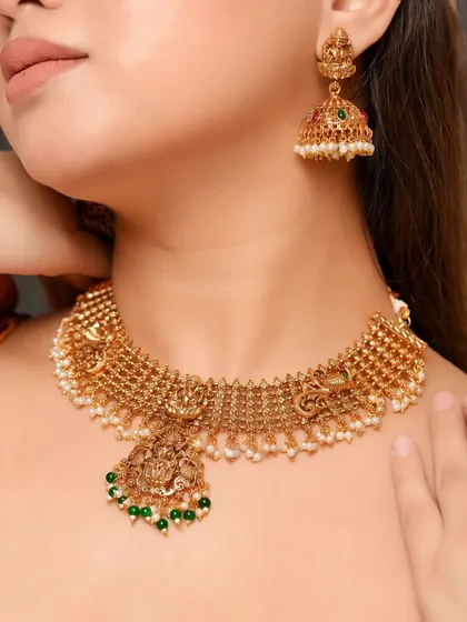 A focused shot on a traditional gold choker necklace with a temple jewelry pendant. The image clearly displays the texture of the gold and the fine details of the design.