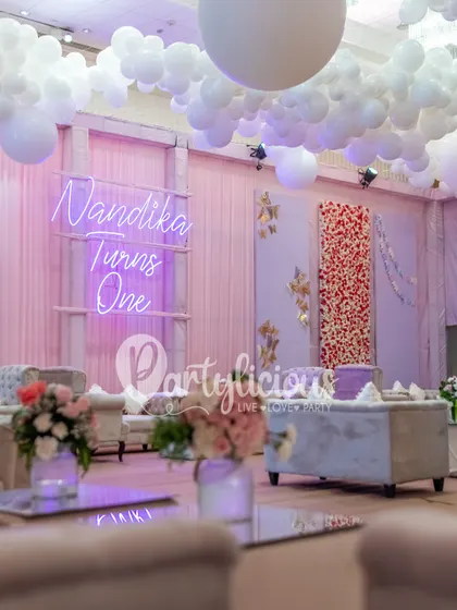 A chic lounge area for a first birthday party, with a custom neon sign, balloon clouds, and comfortable seating.