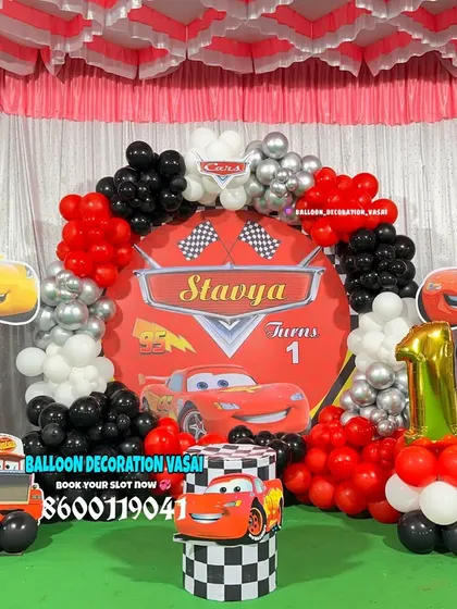A high-energy Disney Cars theme for Stavya's first birthday. This setup features a custom backdrop, character cutouts of Lightning McQueen, and a red, black, and silver balloon arrangement.